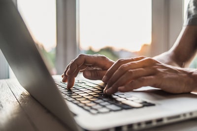 HAnds are seen using a laptop keyboard. 