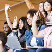 Students in a lecture hall raising their hands