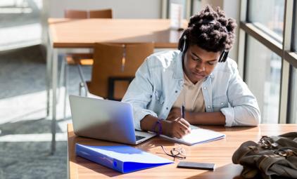 A male African-American student studies at a table in a brightly-lit campus room.