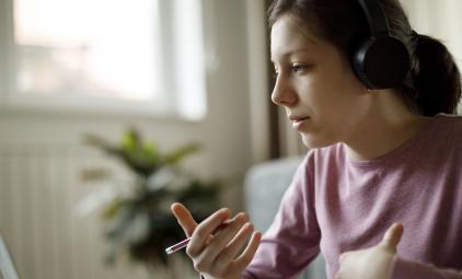 A female, college-aged student wearing headphones looks at her laptop screen.