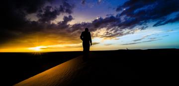 Man walking on dune at sunset.