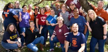 Members of the Dana Center staff gather together wearing shirts representing their various collegiate backgrounds.