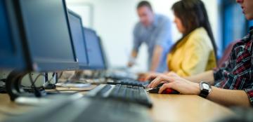 close of on a row of computer keyboards with three out of focus people