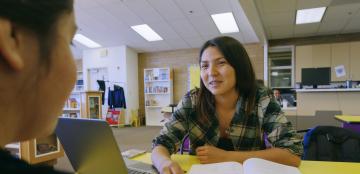 Student at a library table with open books and a laptop