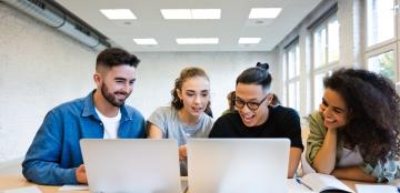 group of students looking at two laptops with papers around them