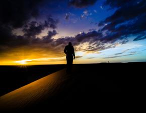 Man walking on dune at sunset.