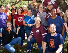 Members of the Dana Center staff gather together wearing shirts representing their various collegiate backgrounds.