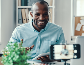 A young African-American male professor smiles into his web camera while teaching an online class.