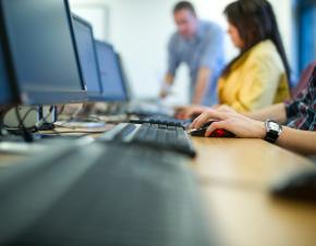 close of on a row of computer keyboards with three out of focus people