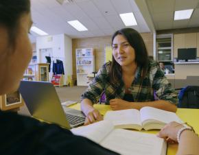 Student at a library table with open books and a laptop