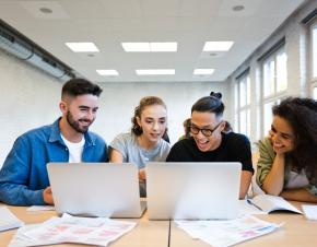 group of students looking at two laptops with papers around them