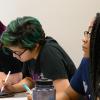 A group of college-aged students sits together at a table in a mathematics classroom. 