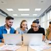 group of students looking at two laptops with papers around them